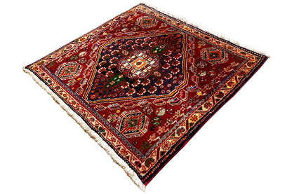 Square rug with a traditional ornamental pattern in shades of red and green, fringes