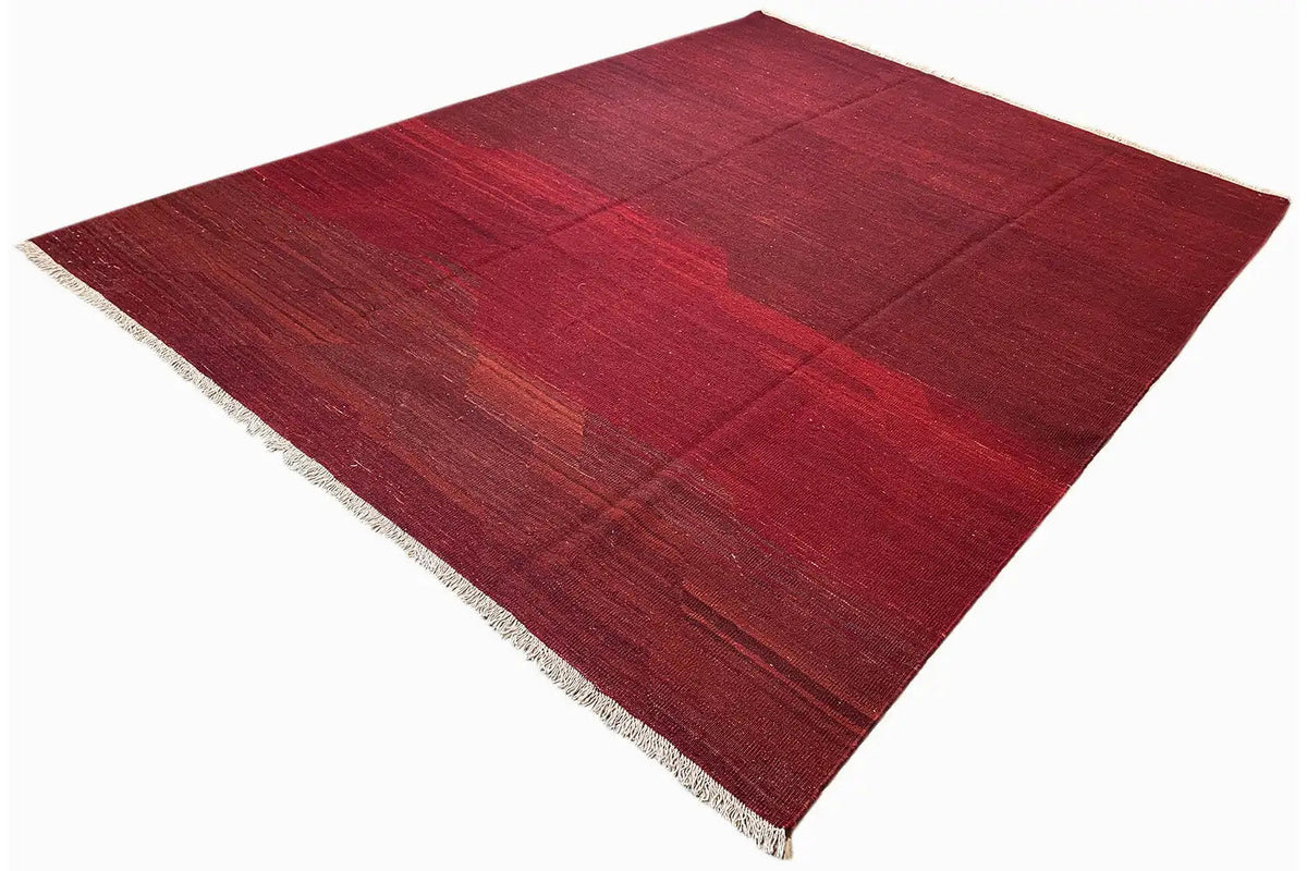 Red kilim rug, diagonal view, with white fringes and a geometric grid pattern