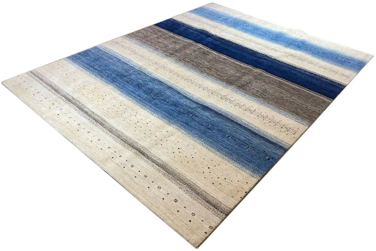 Gabbeh Lori rug at an oblique angle: blue stripes, a gray area, and beige lines.