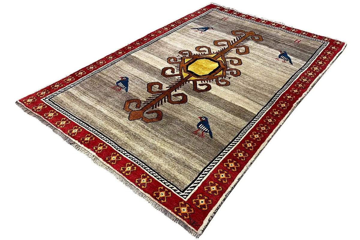 Gabbeh rug laid out: beige background, red border, ornamental tree and birds