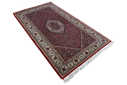 Rug with a burgundy pattern, wide border, and fringe along the bottom edge.