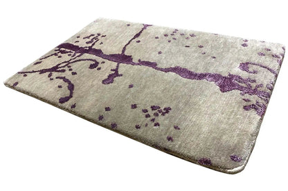 Designer rug laid flat: beige pile with purple ornamental elements