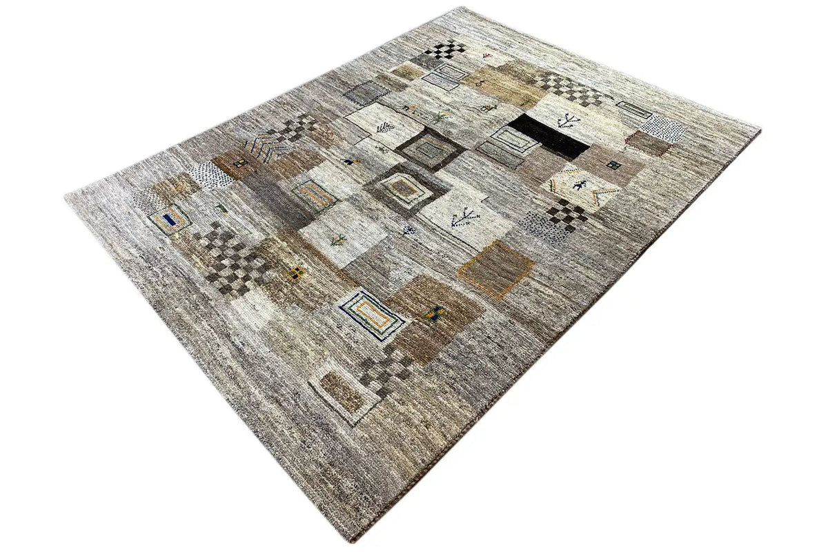 Gabbeh rug photographed at an angle: gray-beige pile with dark and golden patterned squares