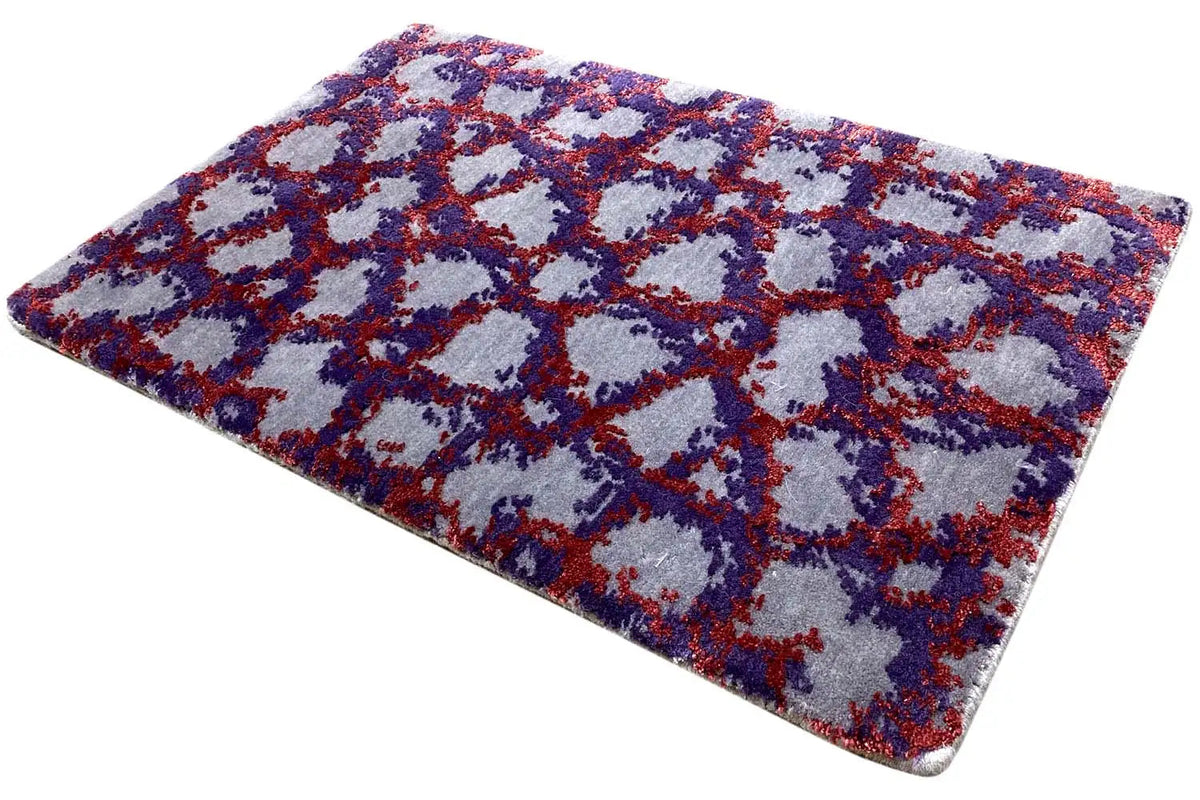 Rectangular rug with a dense pile and abstract pattern in blue, red, and purple.