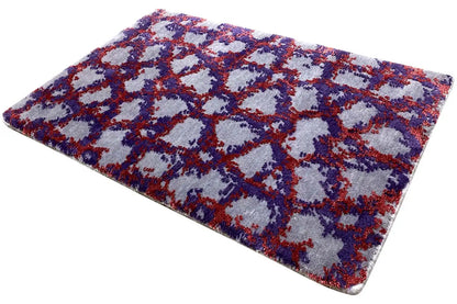 Rectangular rug with a dense pile and abstract pattern in blue, red, and purple.