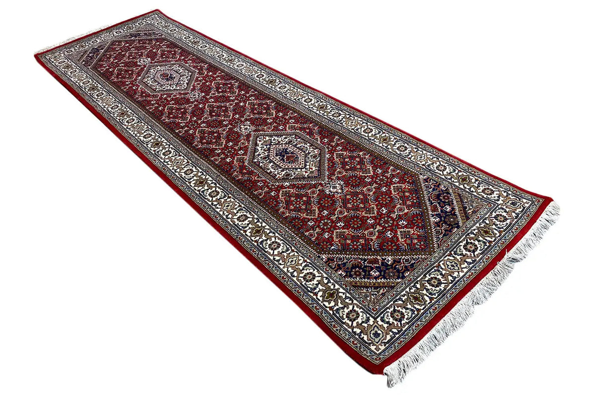 Bidjar runner in triangular view with a red background, ornate border, and fringes.