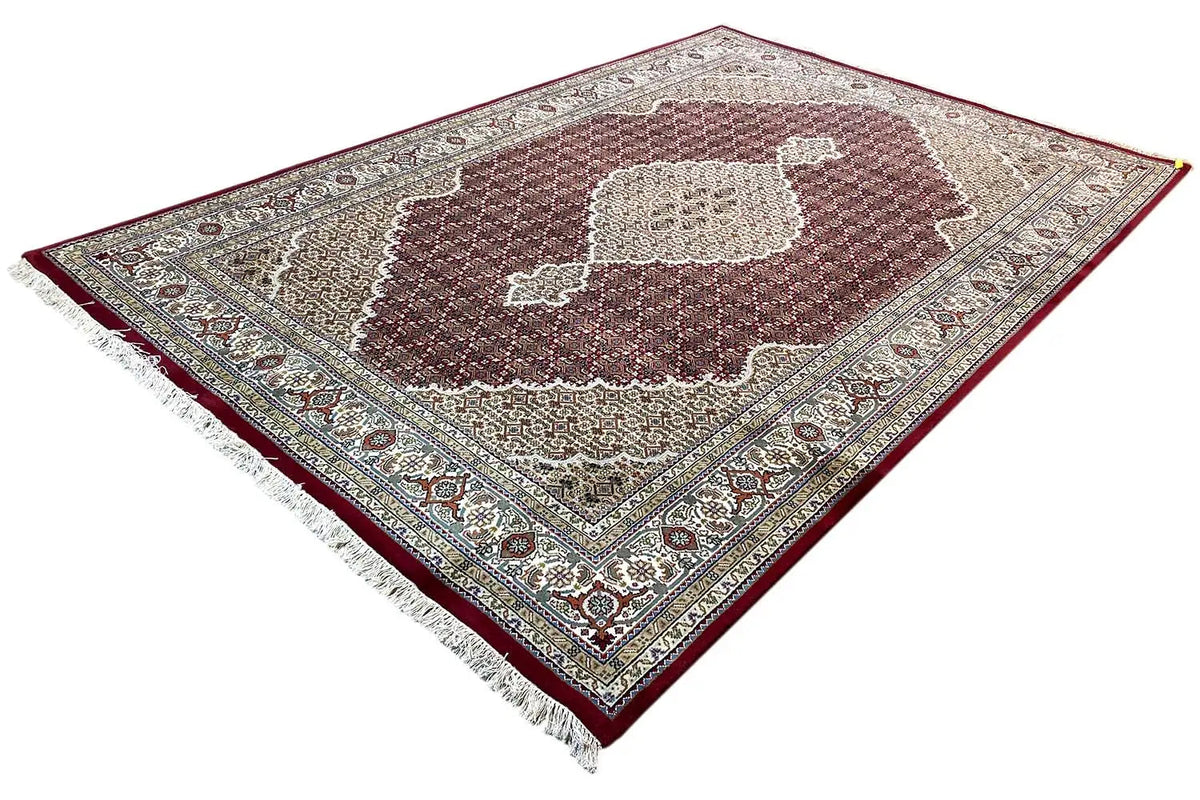 Indo-Tabriz rug at an angle, beige patterned field with a brown center and decorative border