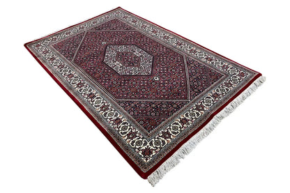 Rug viewed from above at an angle: maroon central field with a central pattern and a wide ornamental border