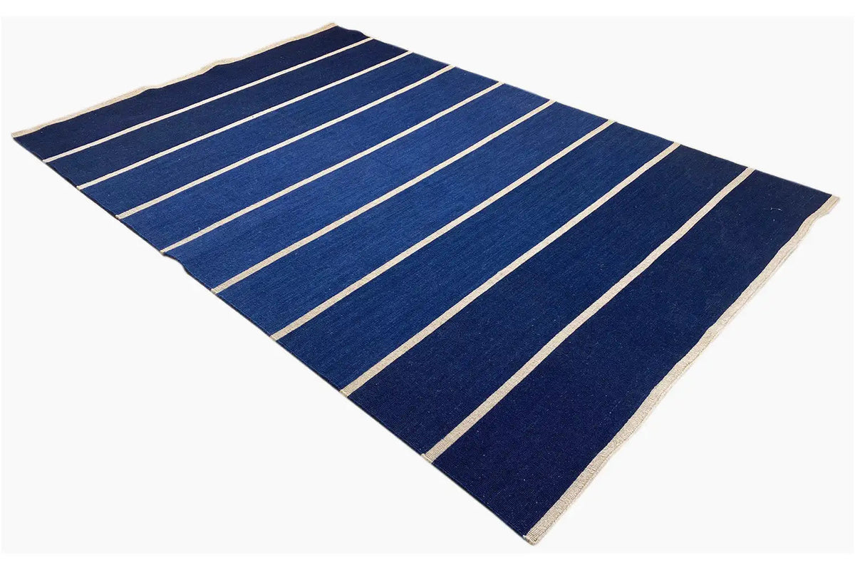 Rectangular kilim with a dark blue field, light stripes, and a beige edge border.