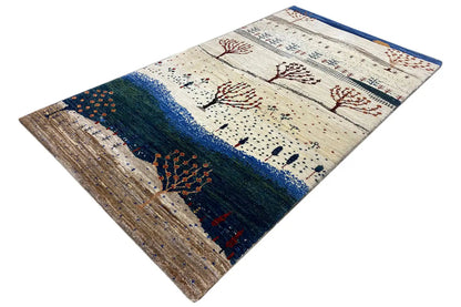 Gabbeh rug at an angle with a blue border, tree motifs, and brown pile
