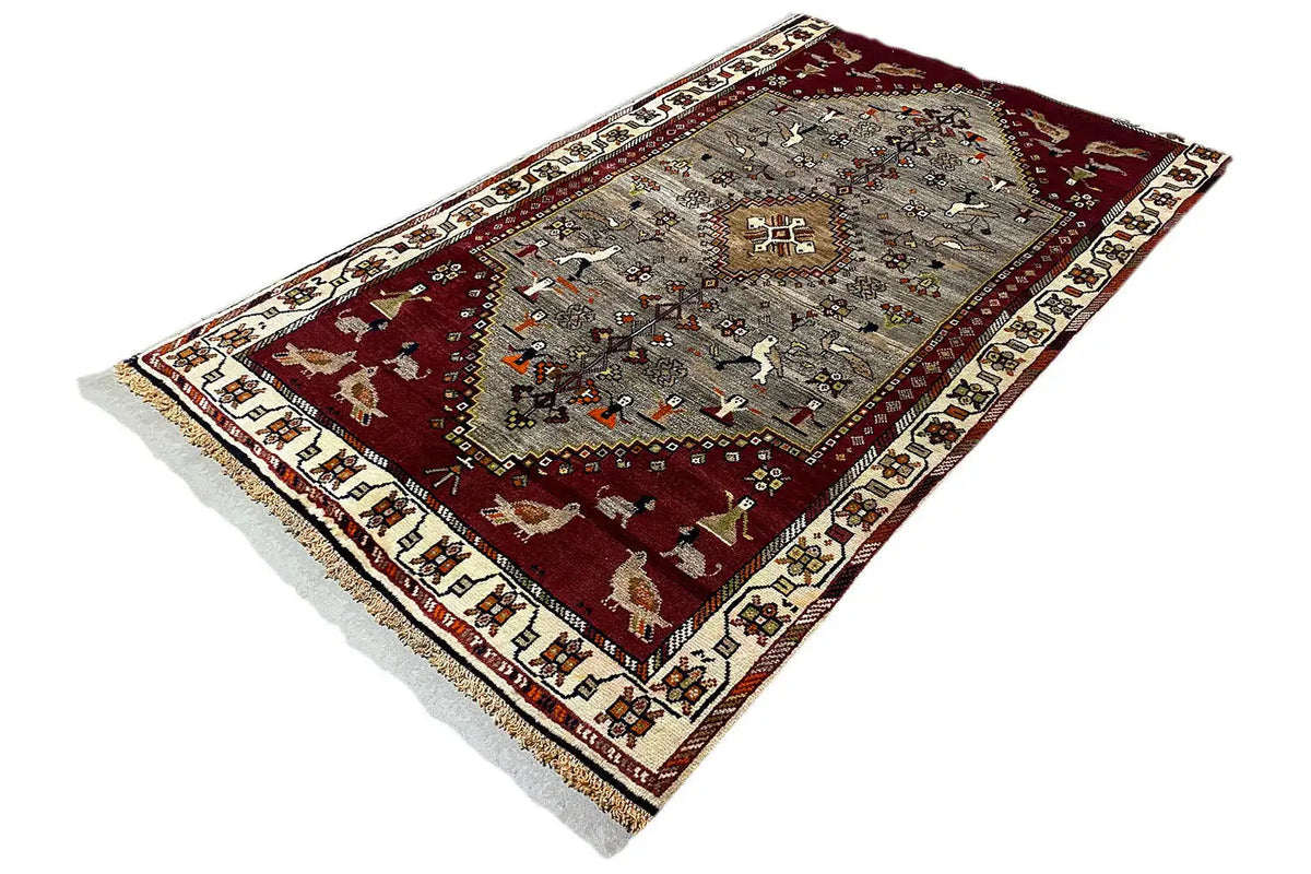 Gabbeh rug in diagonal view, red and gray with a central motif and decorative border
