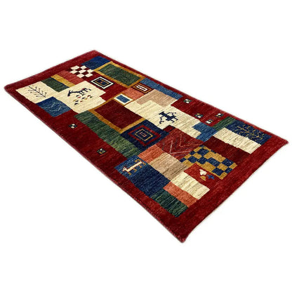Red Gabbeh rug with patchwork and border patterns, viewed diagonally from above.