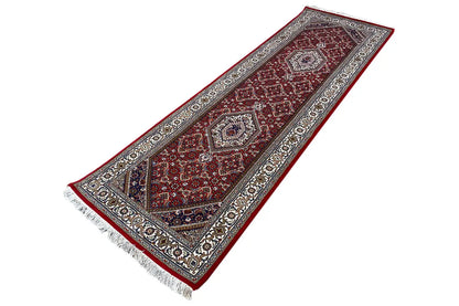Bidjar runner laid flat: red patterned field, light border, and fringe along the edge.