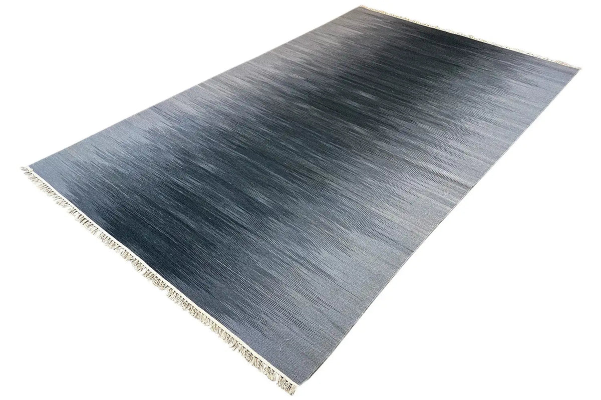 Gray ombré kilim dhurrie rug with fringes, viewed from above at an angle
