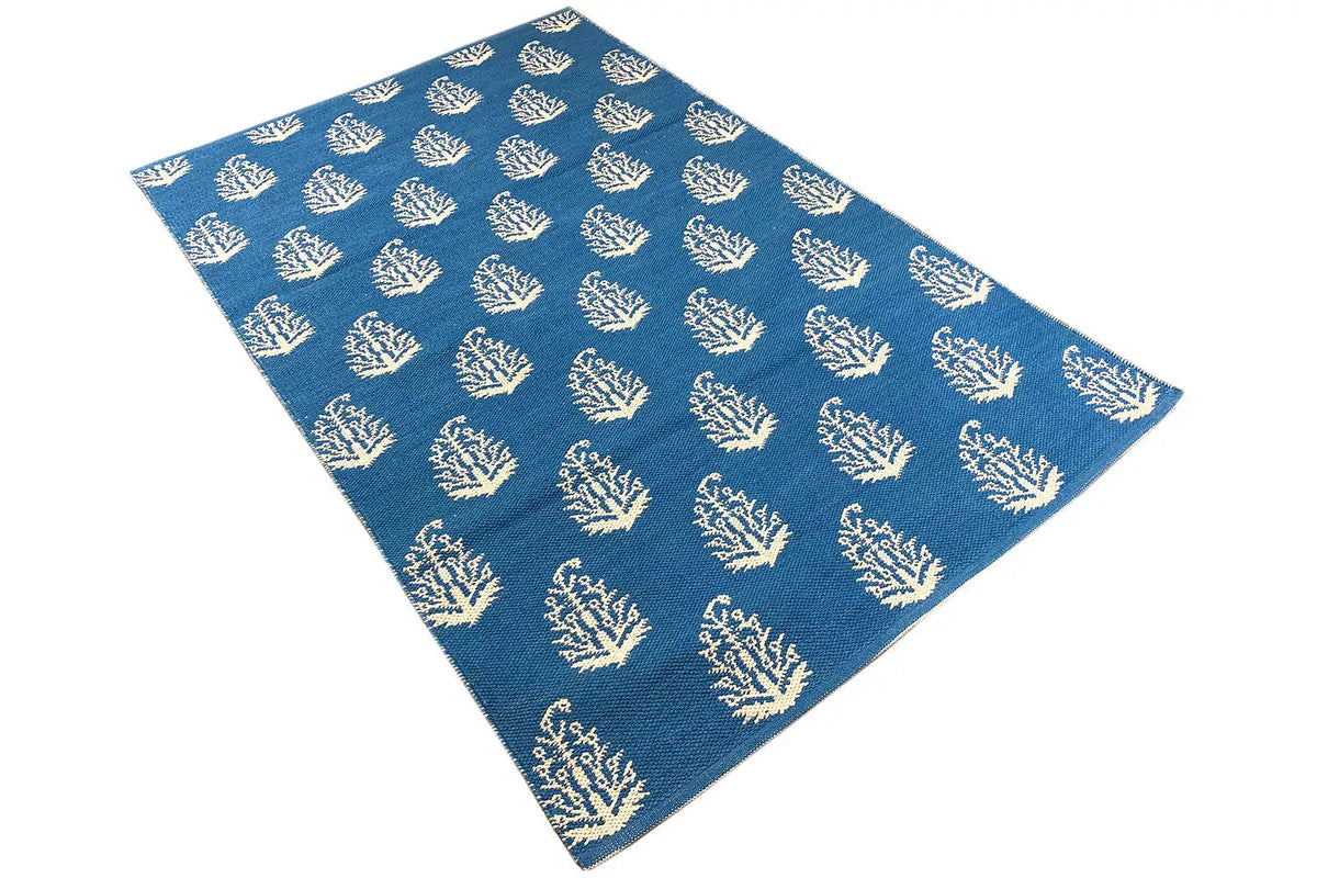 Blue kilim with cream-colored tree/branch motifs, rectangular, photographed diagonally.