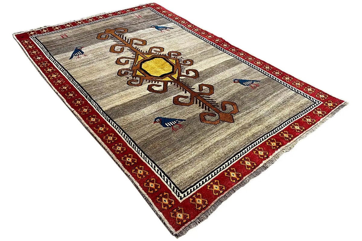 Gabbeh rug at an angle: beige background, red border, golden medallion and ornamental tree