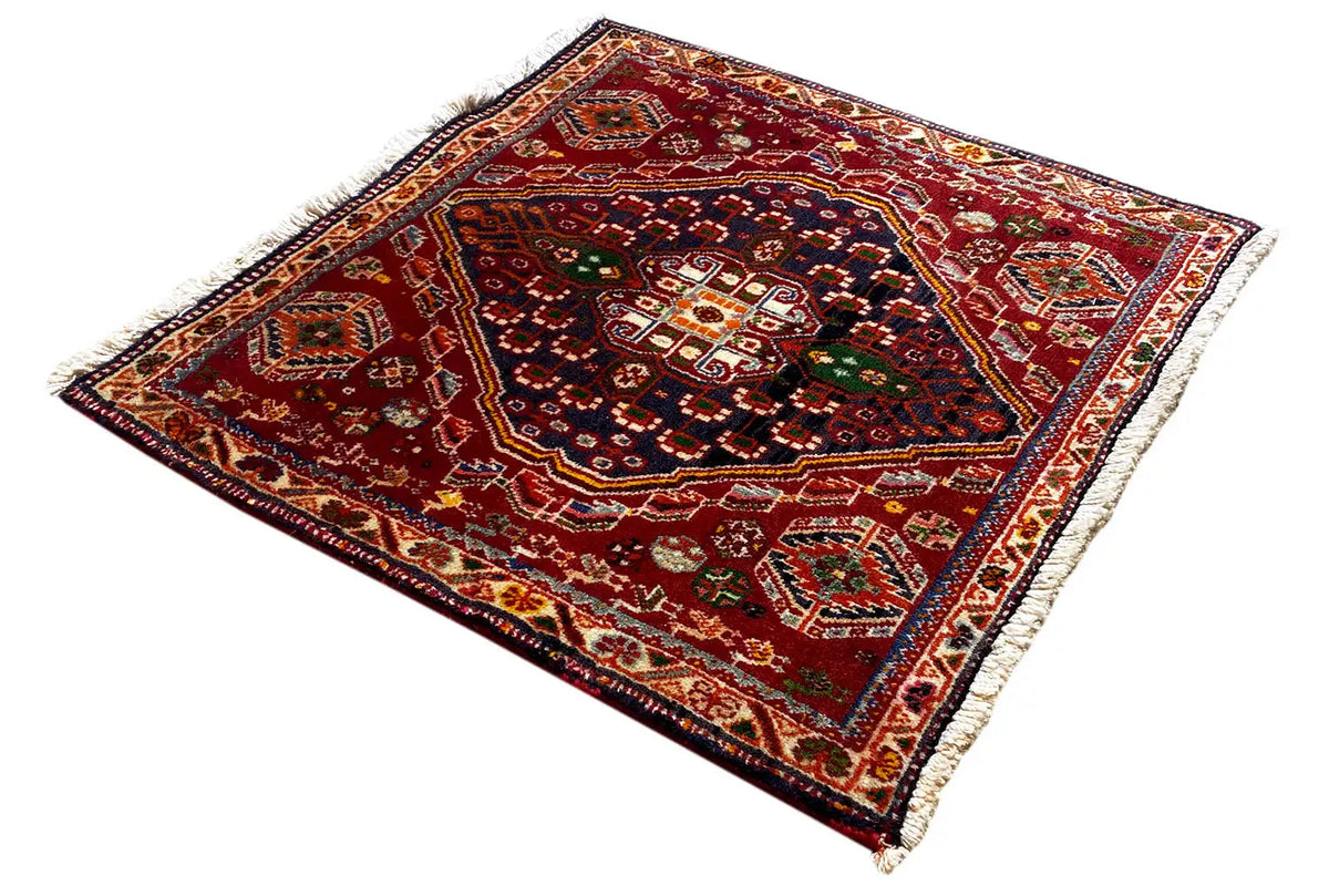 Square rug with red ornamental design, multicolored border, and fringes