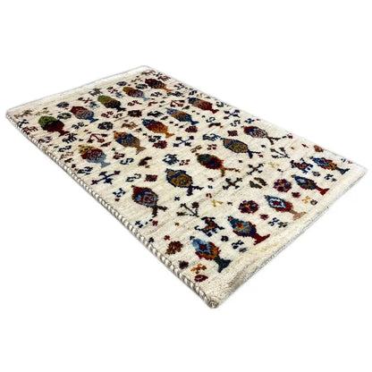 Gabbeh rug 58x37 cm shown at an angle, cream with colorful figures and ornaments.