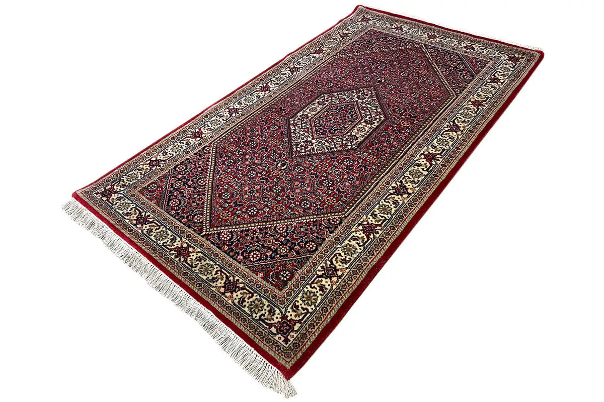 Rug with a red central field, delicate ornamental inlays, and fringes along the edge.