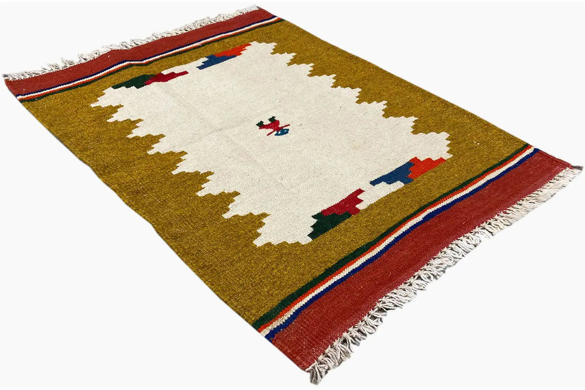 Kilim rug spread out from another perspective, ochre with a white central motif and fringes