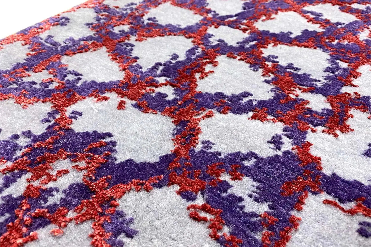 Close-up of carpet pile with abstract motifs in blue, red, and purple on a light background.