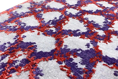 Close-up of carpet pile with abstract motifs in blue, red, and purple on a light background.