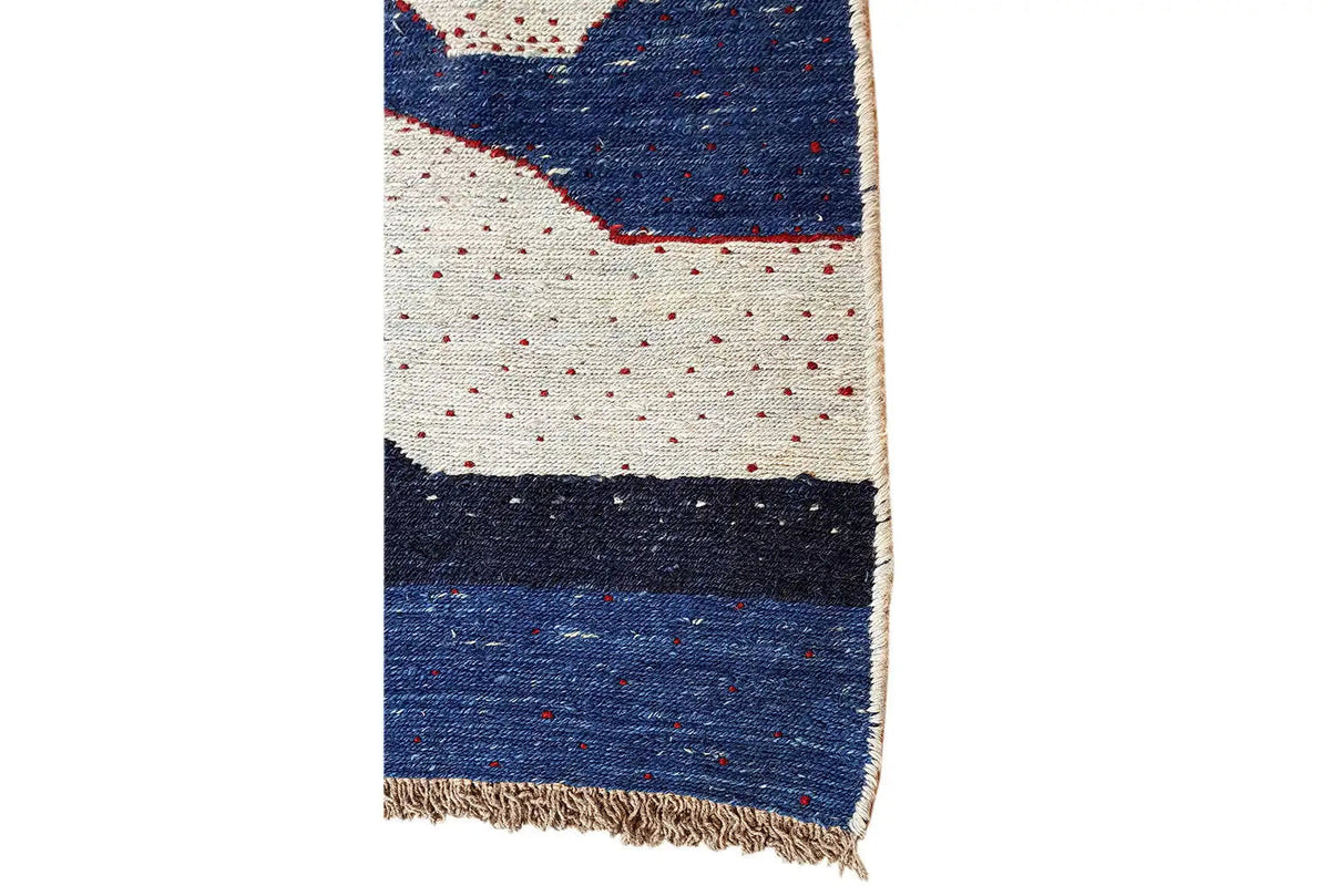 Kilim rug viewed from the side, with fringes and a blue stripe on a light background