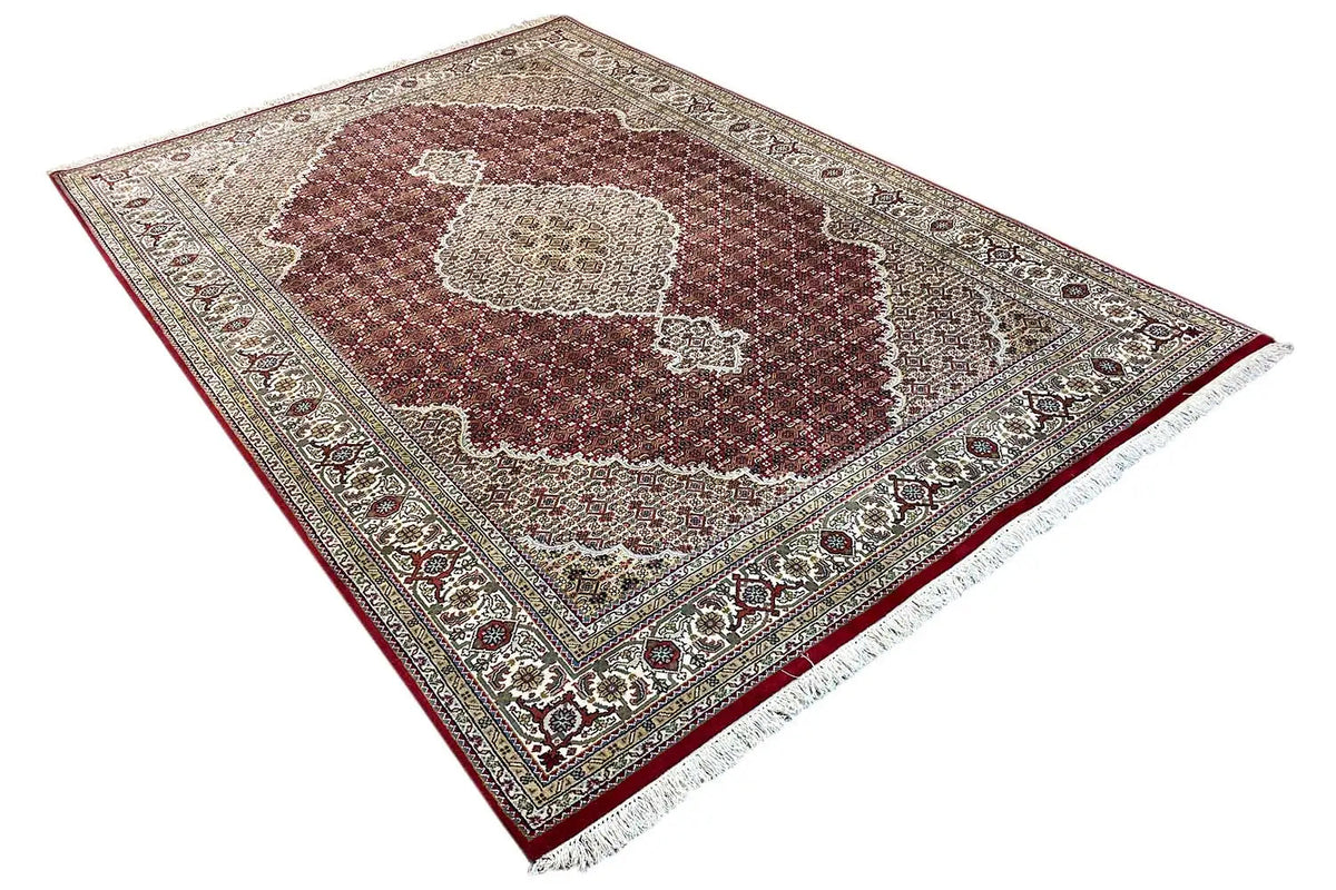 Rug with a maroon medallion, beige ornaments, and fringe at the corner.