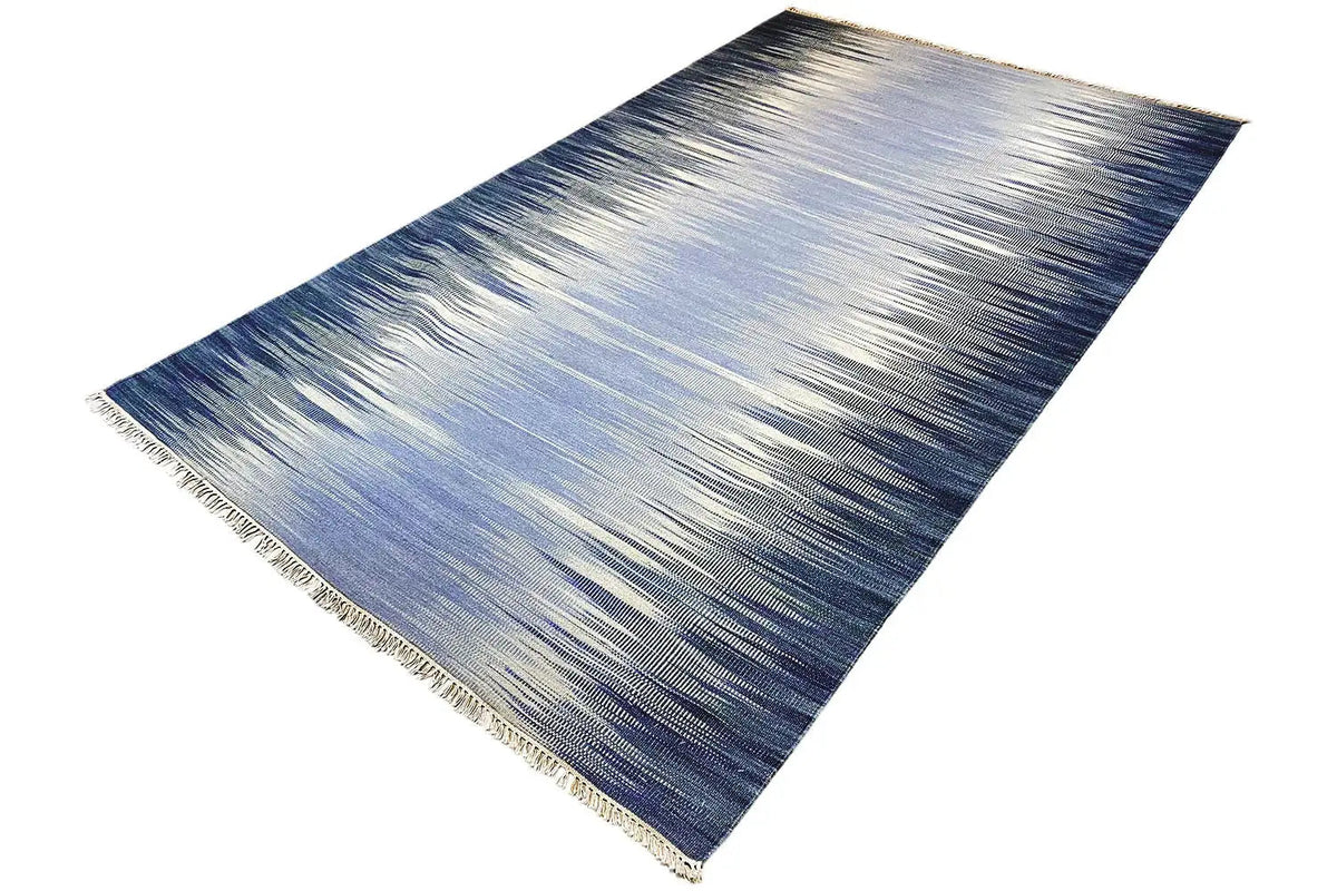 Ombre kelim dhurrie rug in blue and light gray, photographed at an angle, with fringes