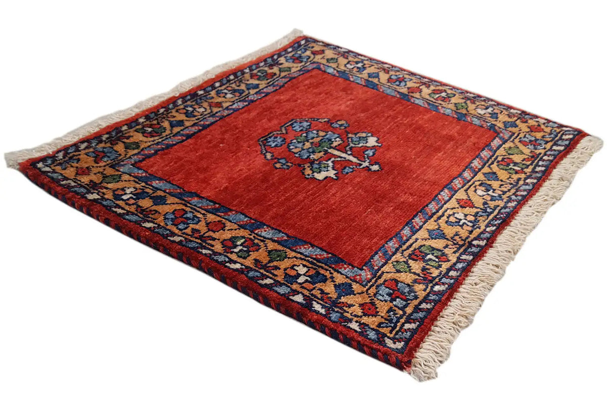 Red patterned rug with a blue border and central floral design, beige fringes