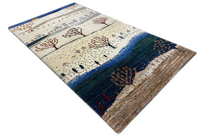 Gabbeh rug lying at an angle with tree motifs, blue border, and beige background