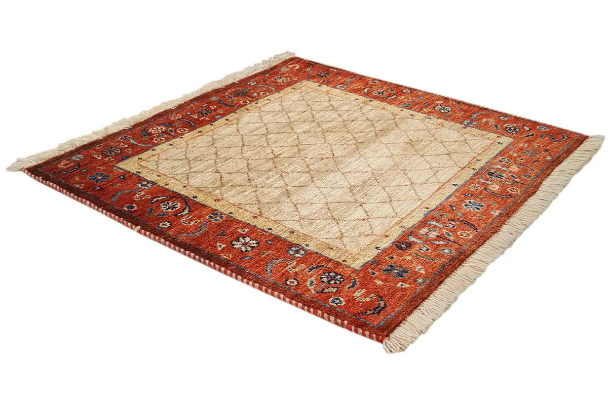 Square carpet in the corner, beige center with a red border pattern and fringes at the corners.