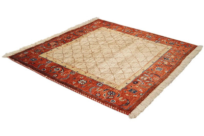 Square carpet in the corner, beige center with a red border pattern and fringes at the corners.