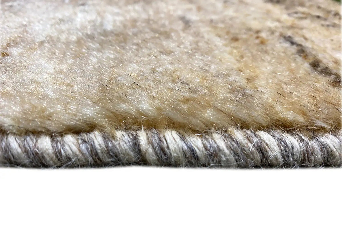 Carpet edge with beige pile and dense fringes; visible gray backing