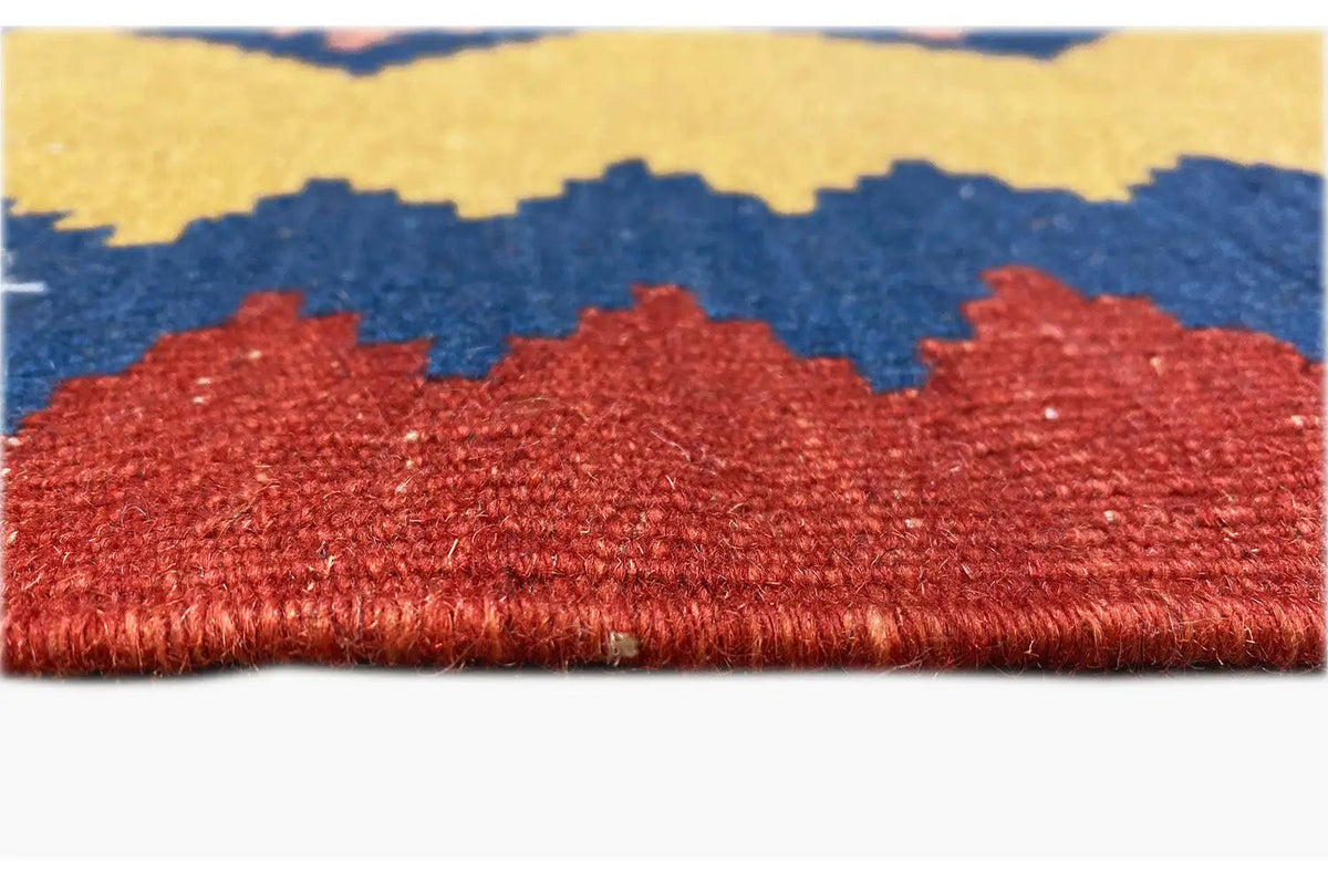 Close-up of a kilim rug: red border with fringes, with blue patterns on a beige background above it