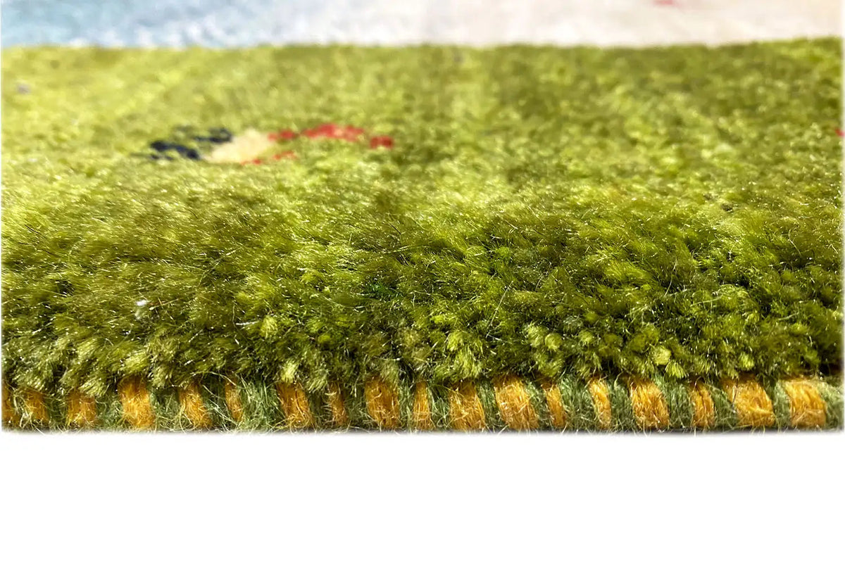 Gabbeh-Lori rug edge view: dense green pile with a colorful border and fringes.