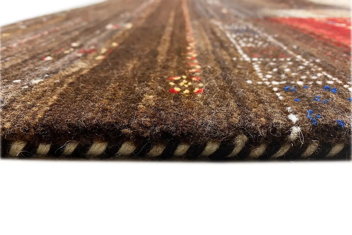 Gabbeh rug edge with fringes and visible weave structure, brown with colorful accents.