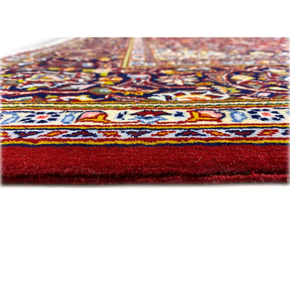 Keshan carpet edge with a fringed border, multicolored trim on a burgundy background.