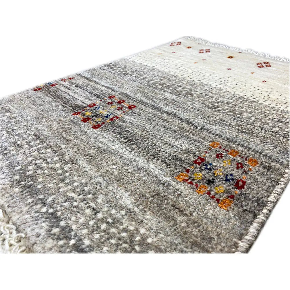 Gabbeh rug close-up: gray texture, colorful motifs, and knotted fringes