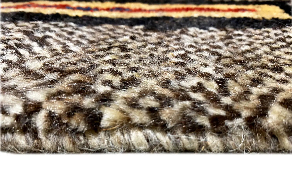 Rug pile in detail: woven texture in beige, brown, and dark tones on a light background.
