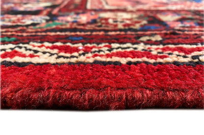 Carpet pile in close-up: dense red pile with multicolored decorative bands along the edge