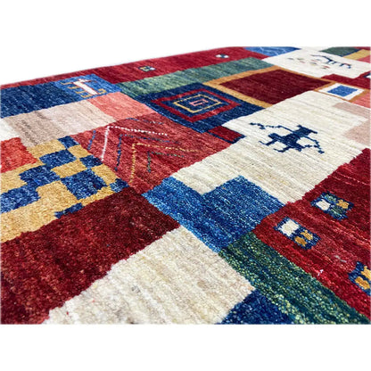 Close-up view of Gabbeh rug: dense pile with a patchwork design in red, blue, and cream.
