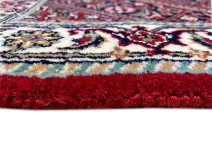 Rug edge with fringe and red pile, above it a multicolored ornamental pattern