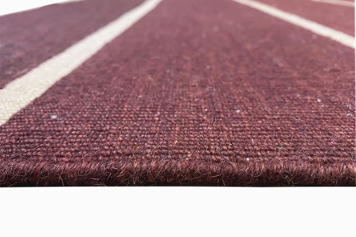 Close-up of the Kelim: wine-red pile with white stripes and a visible edge