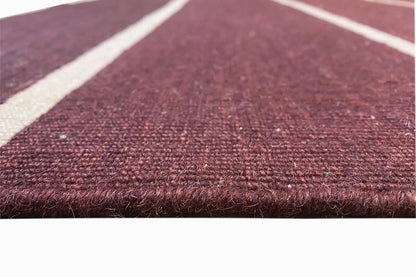 Close-up of the Kelim: wine-red pile with white stripes and a visible edge