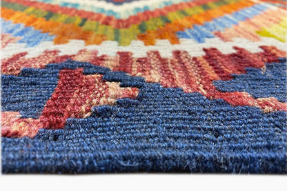 Close-up of a kilim runner: multicolored embroidered texture, blue border band, and reddish patterns