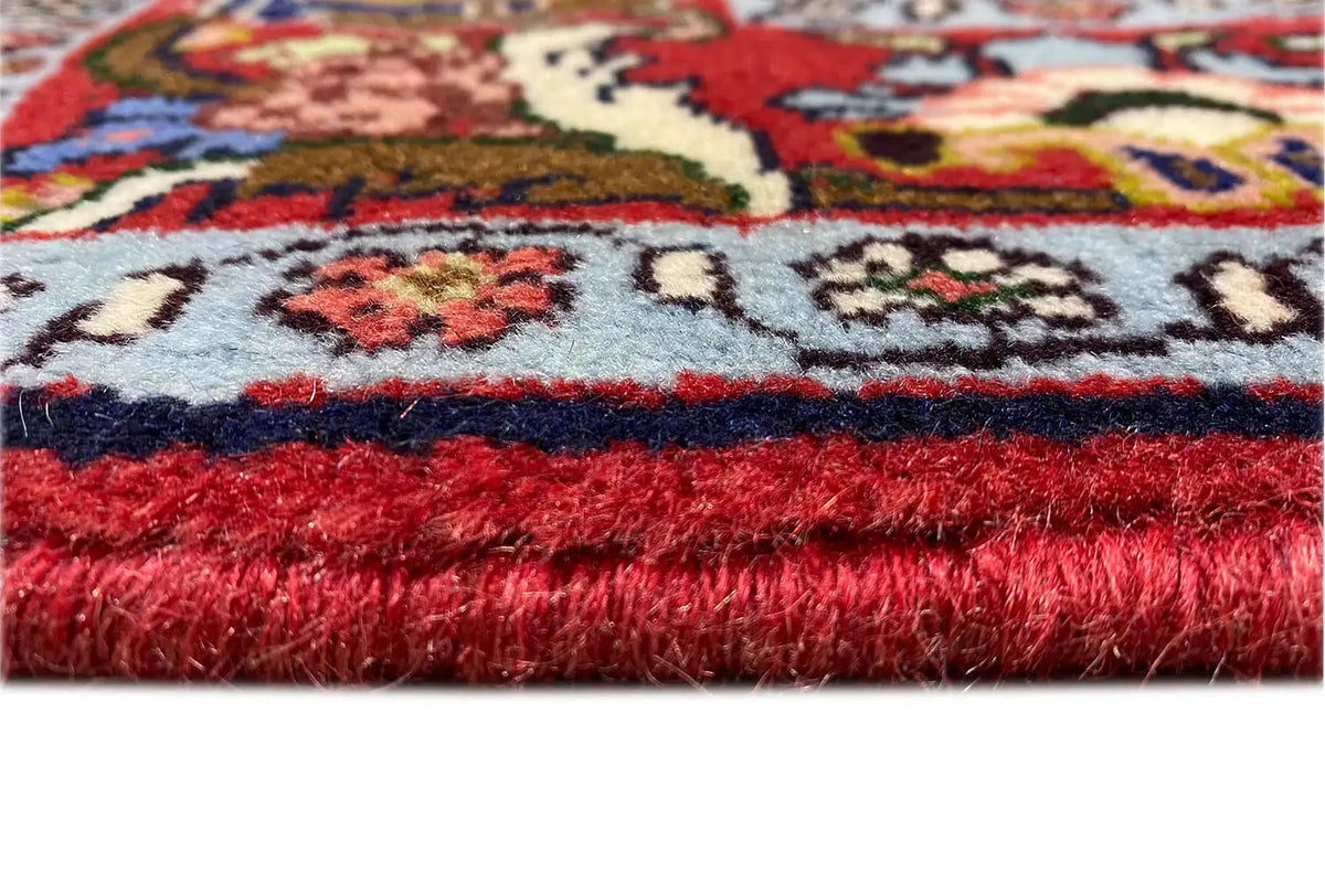 Hamadan carpet edge view with a red pile and white fringes.