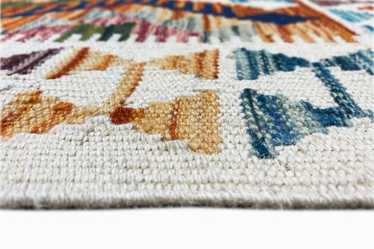 Close-up of a kilim rug with a woven edge, white stitches, and colorful patterns