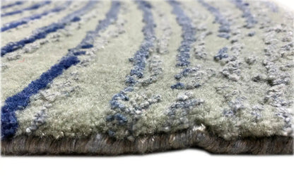 Designer rug with light gray pile and dark blue stripes; visible edge with fringes