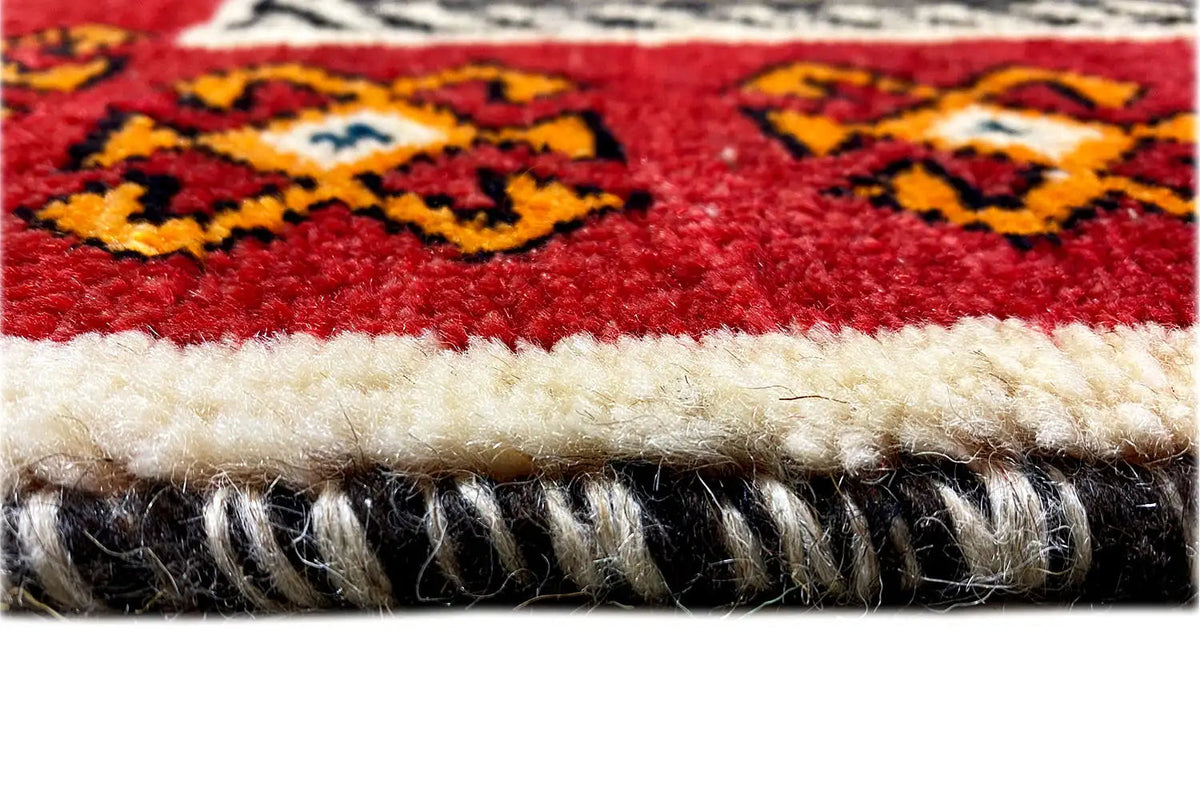 Rug edge with a dense fringed border, red-and-beige pattern, and fine pile surface